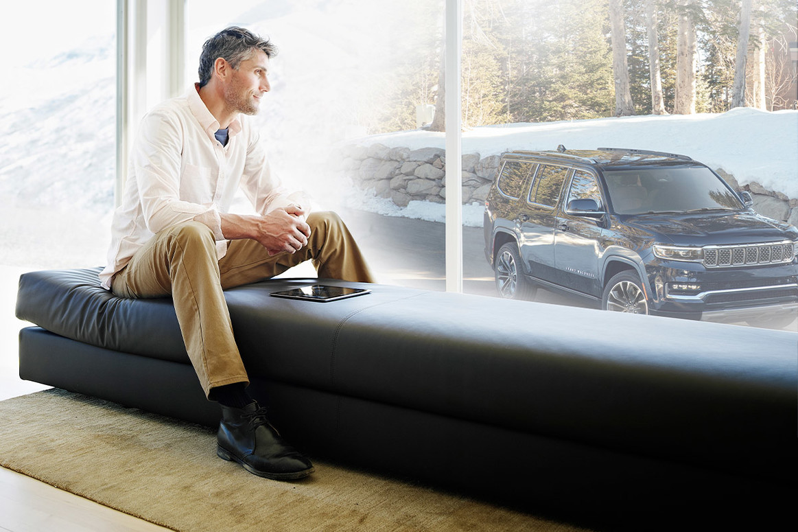 A view of a person staring out a large window with a black 2024 Wagoneer shown parked outside.
