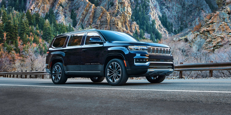 Vue de profil d’un Grand Wagoneer 2024 noir garé sur une route pavée avec une glissière de sécurité et des montagnes visibles au loin.