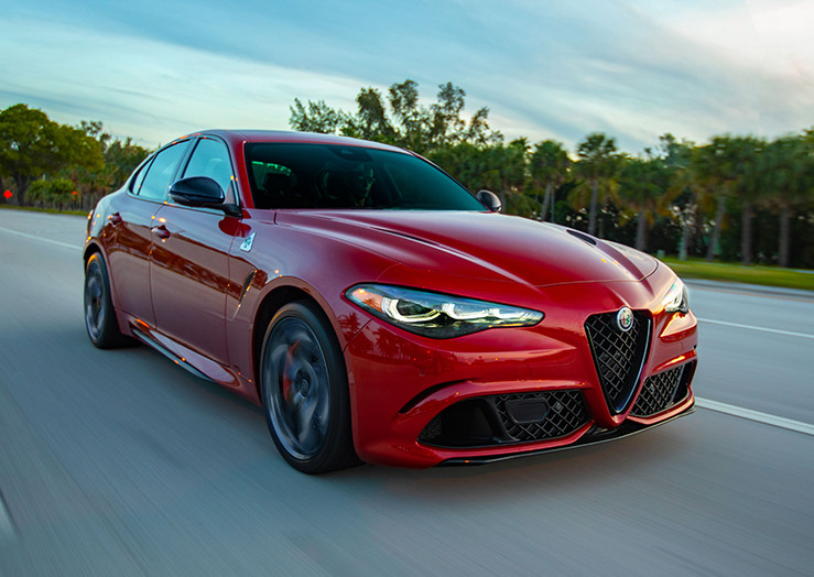 The side of a red 2024 Alfa Romeo Guilia driving down an open road with blurry trees on both sides.