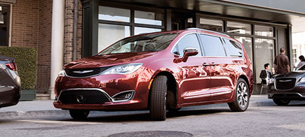 Mini-fourgonnette Chrysler rouge, qui effectue un stationnement parallèle sur le côté de la route entre deux véhicules.