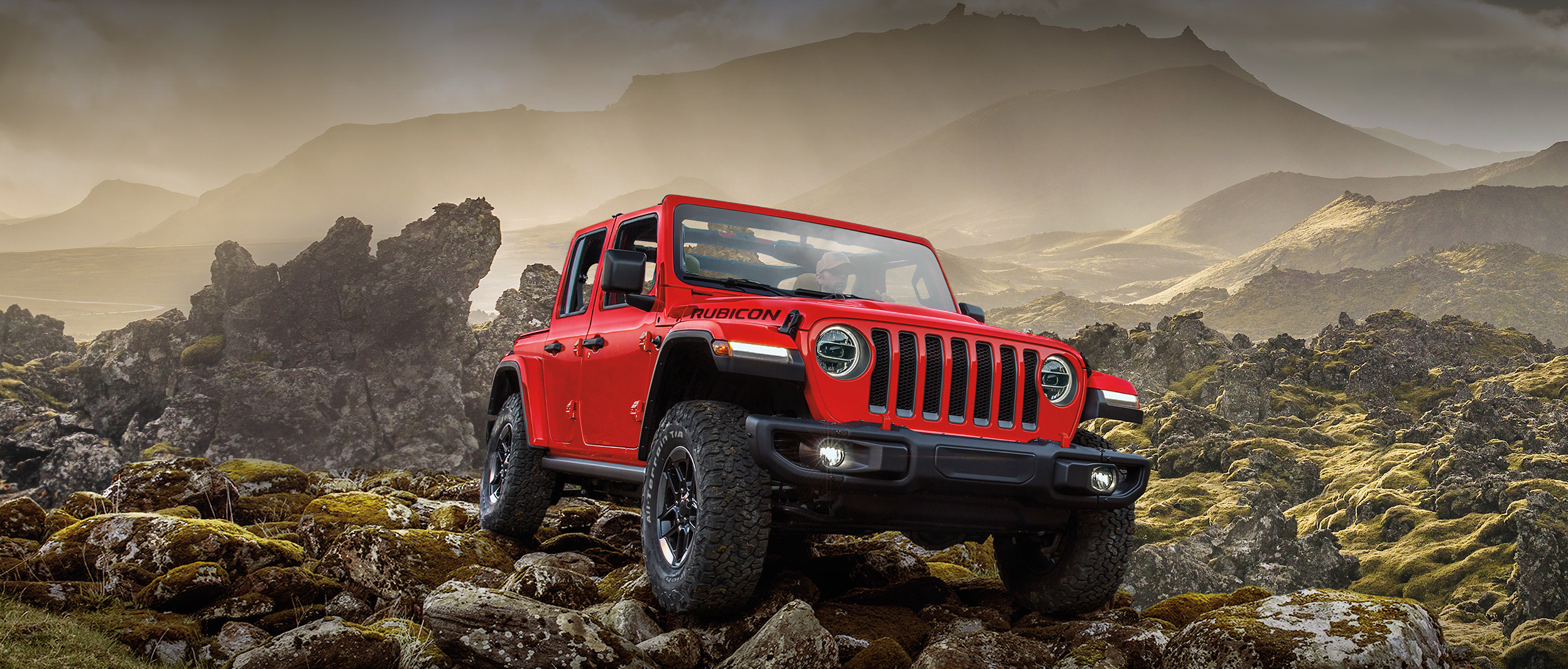 A red Jeep Wrangler driving through rocky terrain
