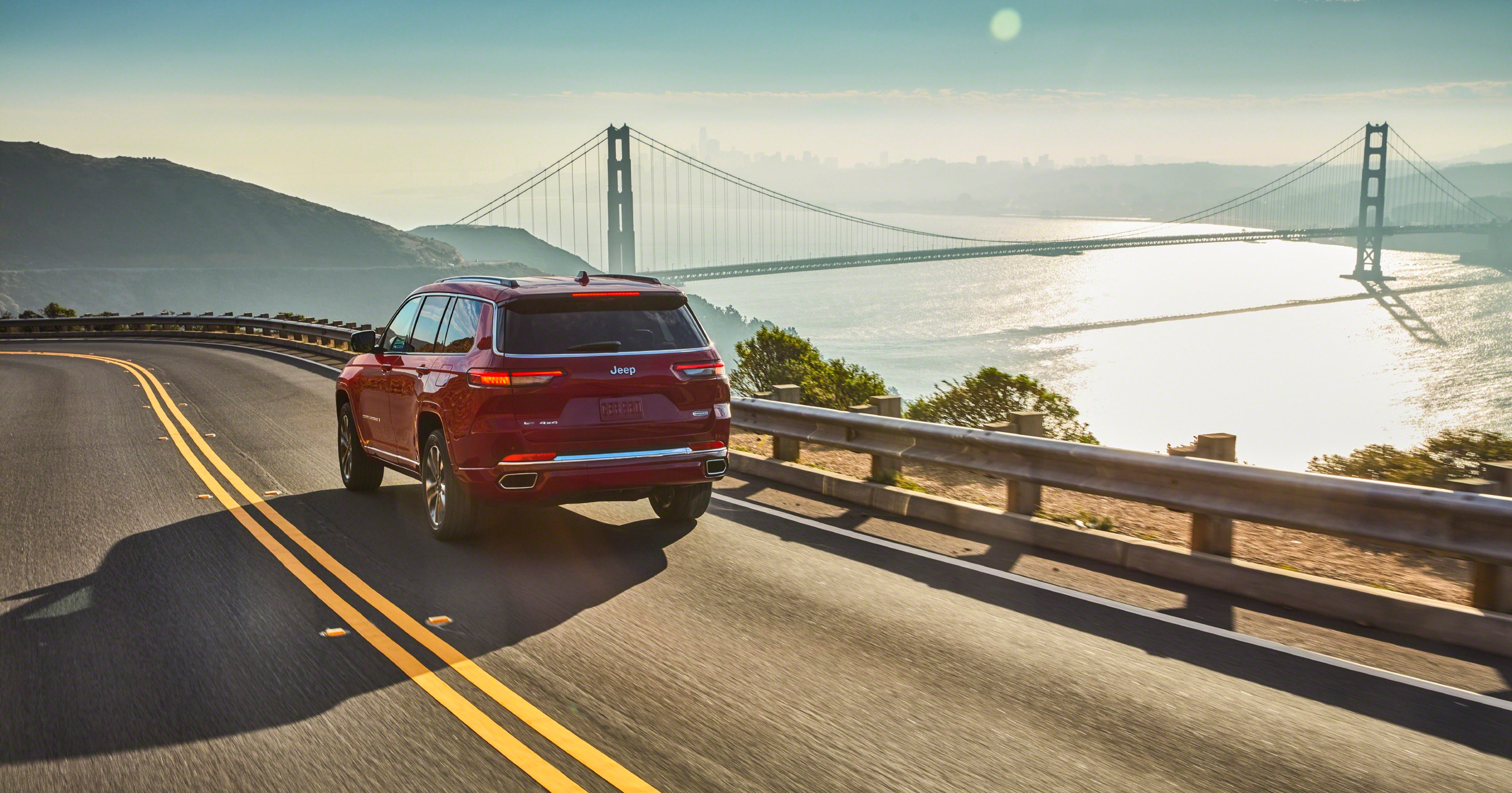 Rear view of a red Jeep driving with a view of the Golden Gate bridge up ahead.