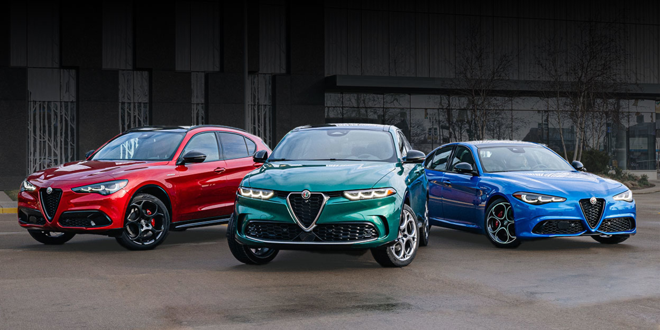 Three Alfa Romeo vehicles parked close to one another in an empty lot outside of a building.