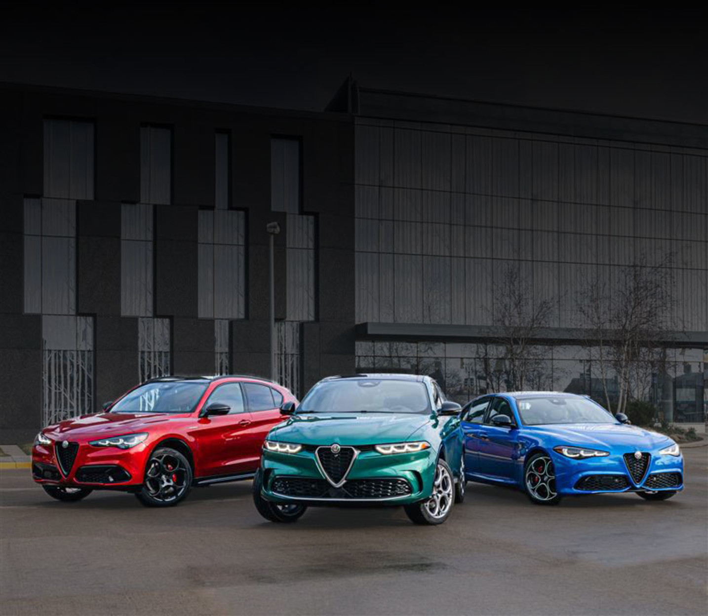 Three Alfa Romeo vehicles parked close to one another in an empty lot outside of a building.