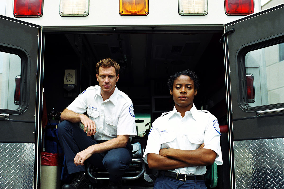 Male and female frontline services paramedics in uniform ready for emergency healthcare services by an open ambulance.
