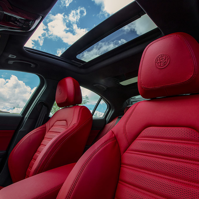 Upward interior view of the 2021 Alfa Romeo Giulia with red front leathers and panoramic sunroof showing clear skies