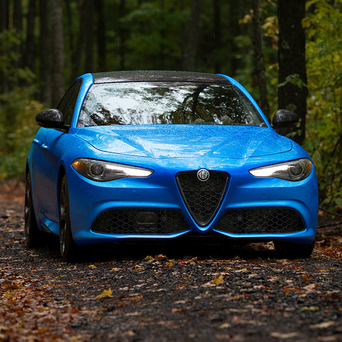 A front view of a blue 2021 Alfa Romeo Giulia being driven through a forest