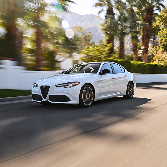 A white 2023 Alfa Romeo Giulia driving down a road with trees in the background.