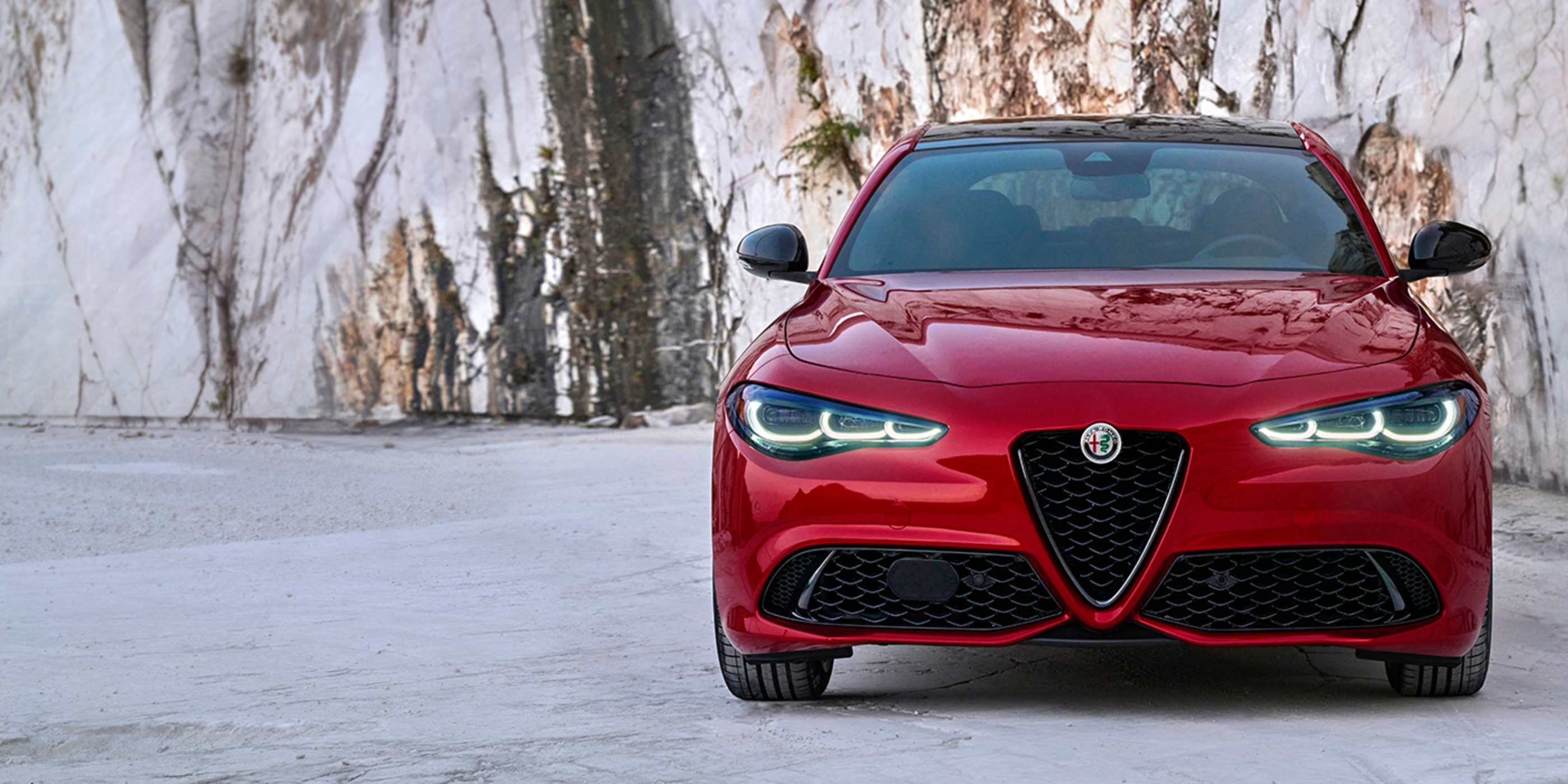 A front view of a red 2024 Alfa Romeo Giulia parked against a rocky-shaped background.