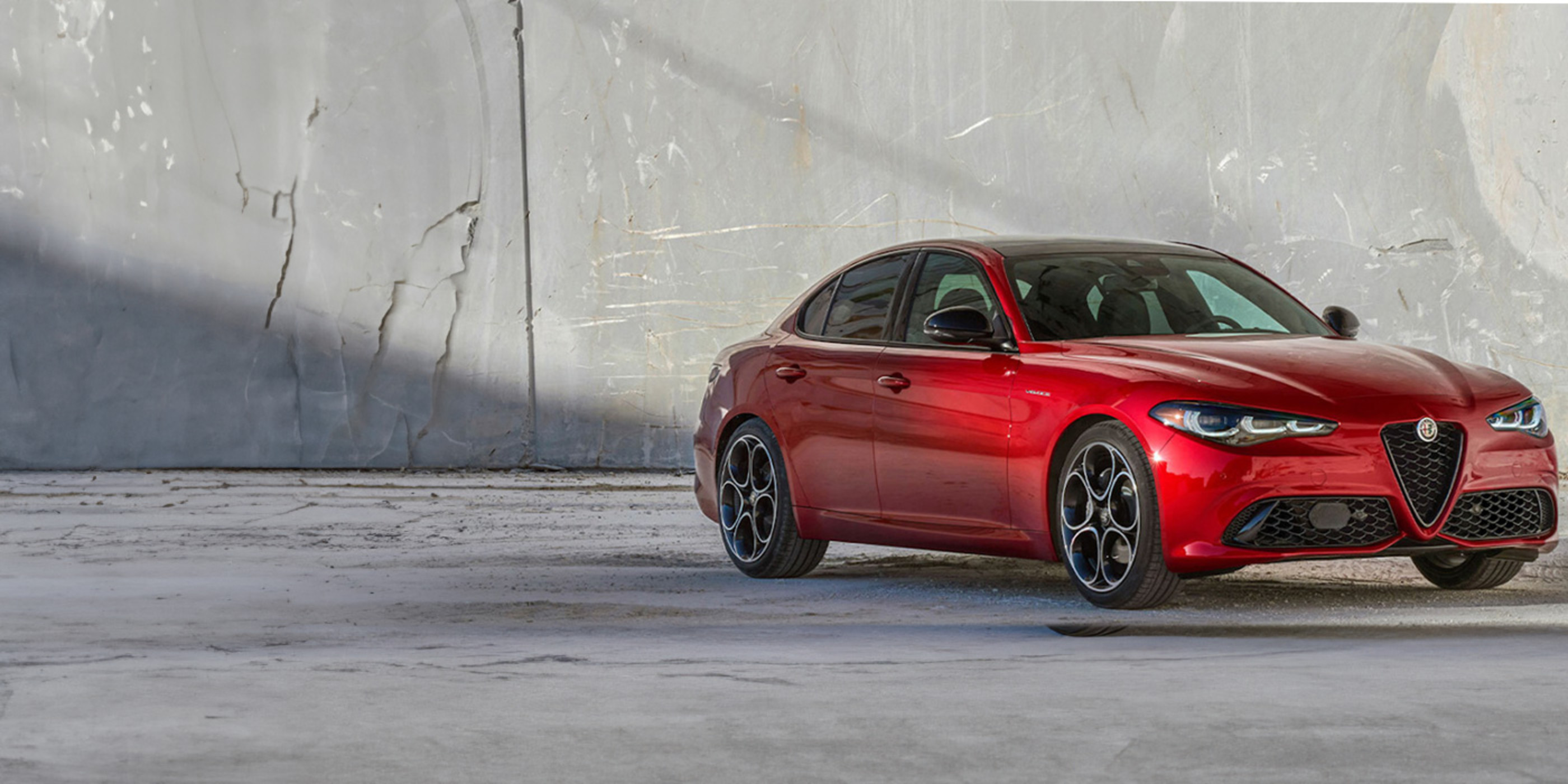 Une Alfa Romeo Giulia rouge 2025 sur une route ouverte au crépuscule. La vue de face met en valeur la calandre distinctive de la voiture et ses phares élégants.