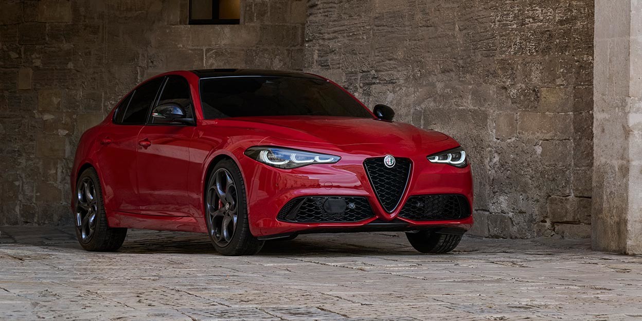 2025 Alfa Romeo Giulia in Alfa Rosso color parked on a cobblestone street under a stone arch. Discover Tributo