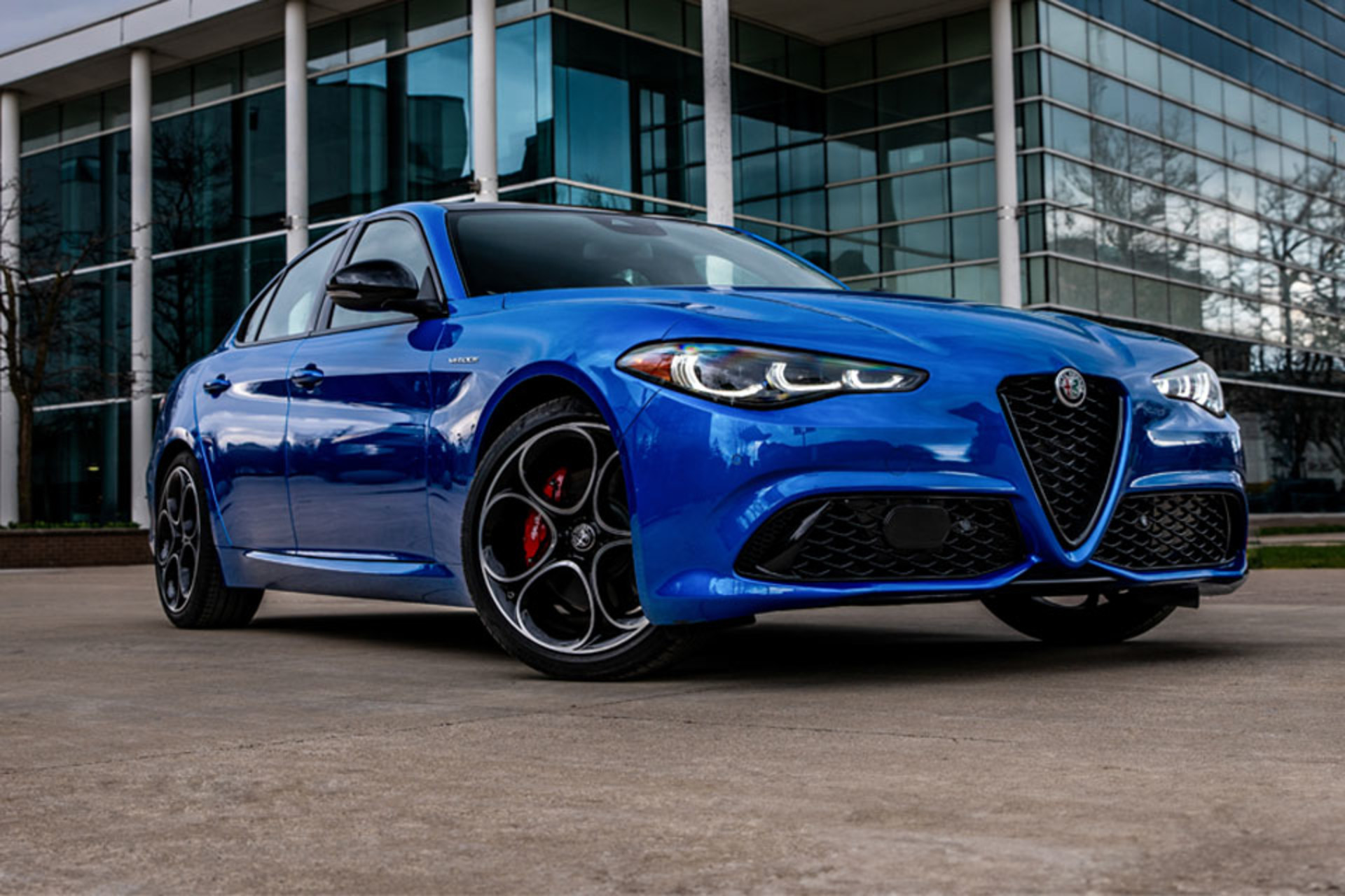 Anodized Blue Metallic 2025 Alfa Romeo Giulia parked in front of a modern glass building.