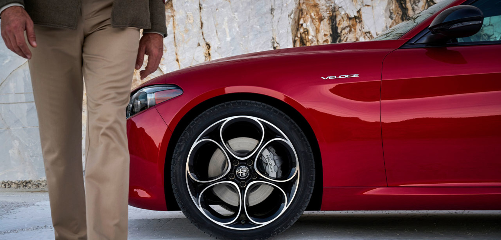 Close-up of a 2025 Alfa Rosso Alfa Romeo Giulia, highlighting part of the right front wing and a person walking away from it.