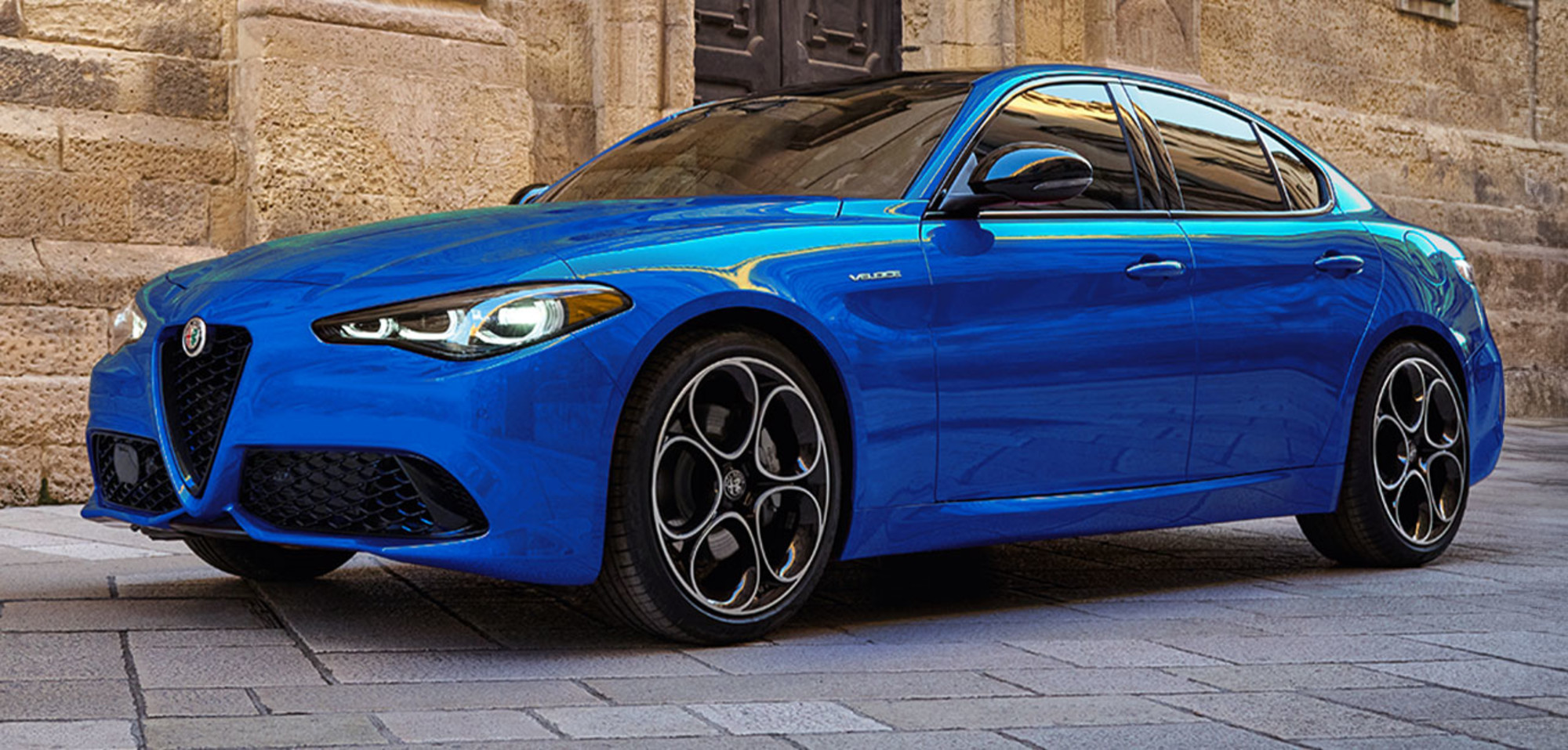 Anodized Blue Metallic 2025 Alfa Romeo Giulia parked on a cobblestone street with stone buildings in the background.