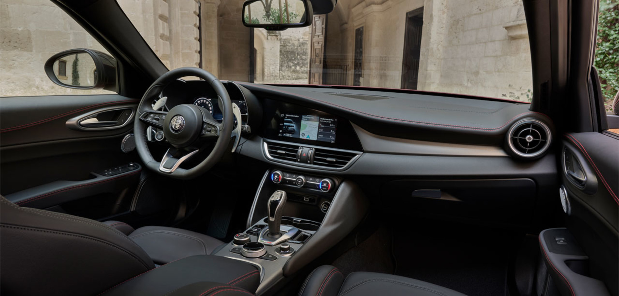 Interior of a 2025 Alfa Romeo Giulia, featuring a modern dashboard and infotainment system, with a view of an architectural structure through the windows.