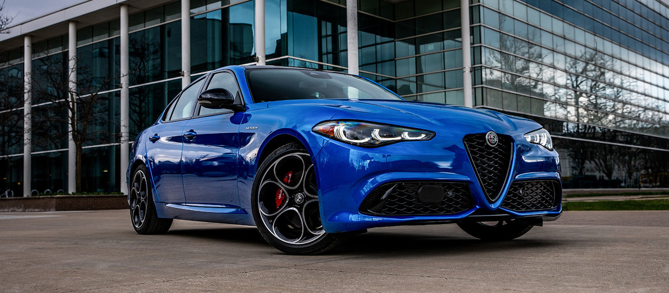 Anodized Blue Metallic 2025 Alfa Romeo Giulia parked in front of a modern glass building.
