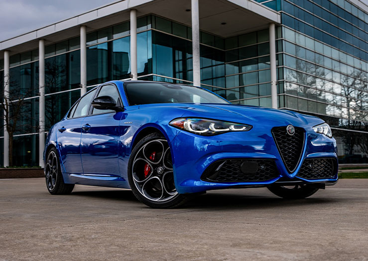 Anodized Blue Metallic 2025 Alfa Romeo Giulia parked in front of a modern glass building.