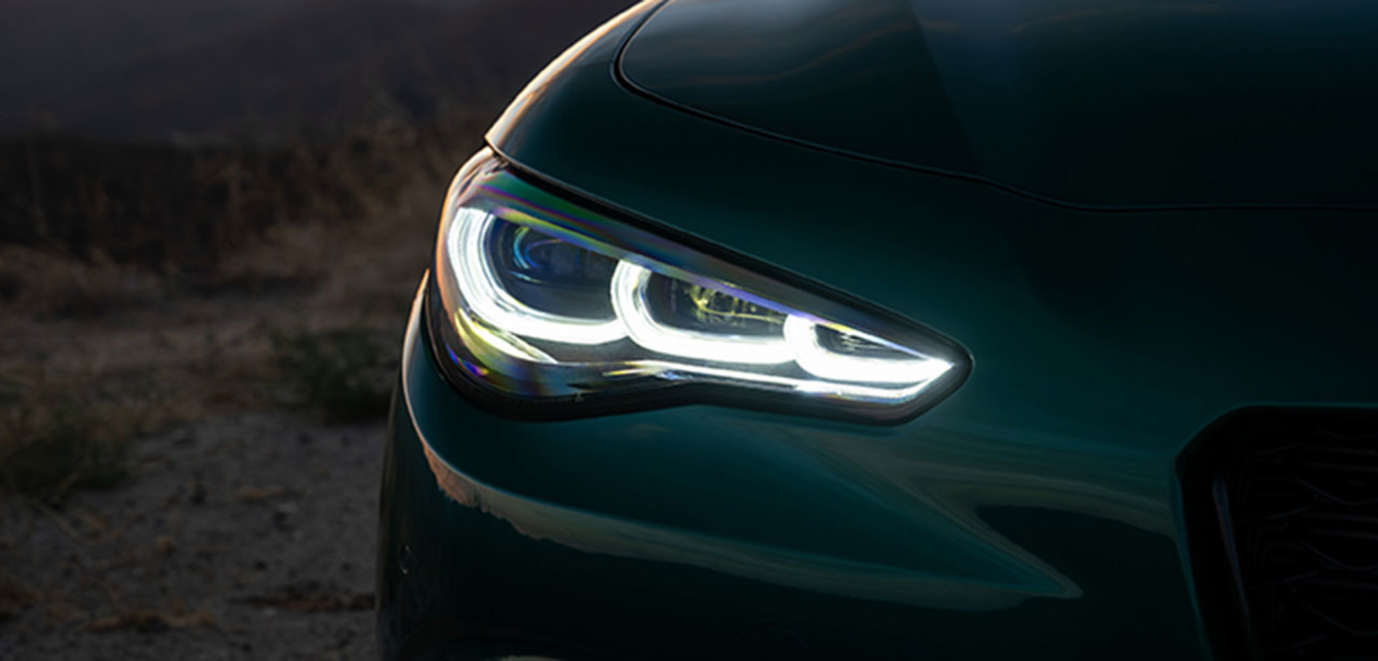 Headlight of a green 2026 Alfa Romeo Giulia at sunset with a scenic mountain backdrop.