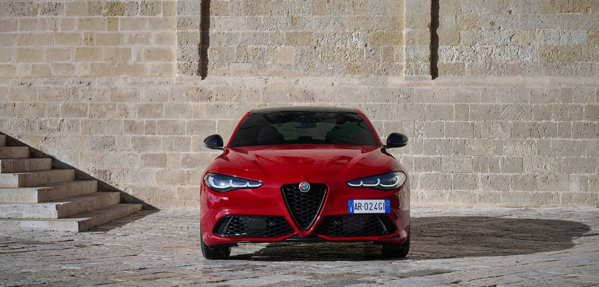 Red 2026 Alfa Romeo Giulia parked in front of a historic stone wall.