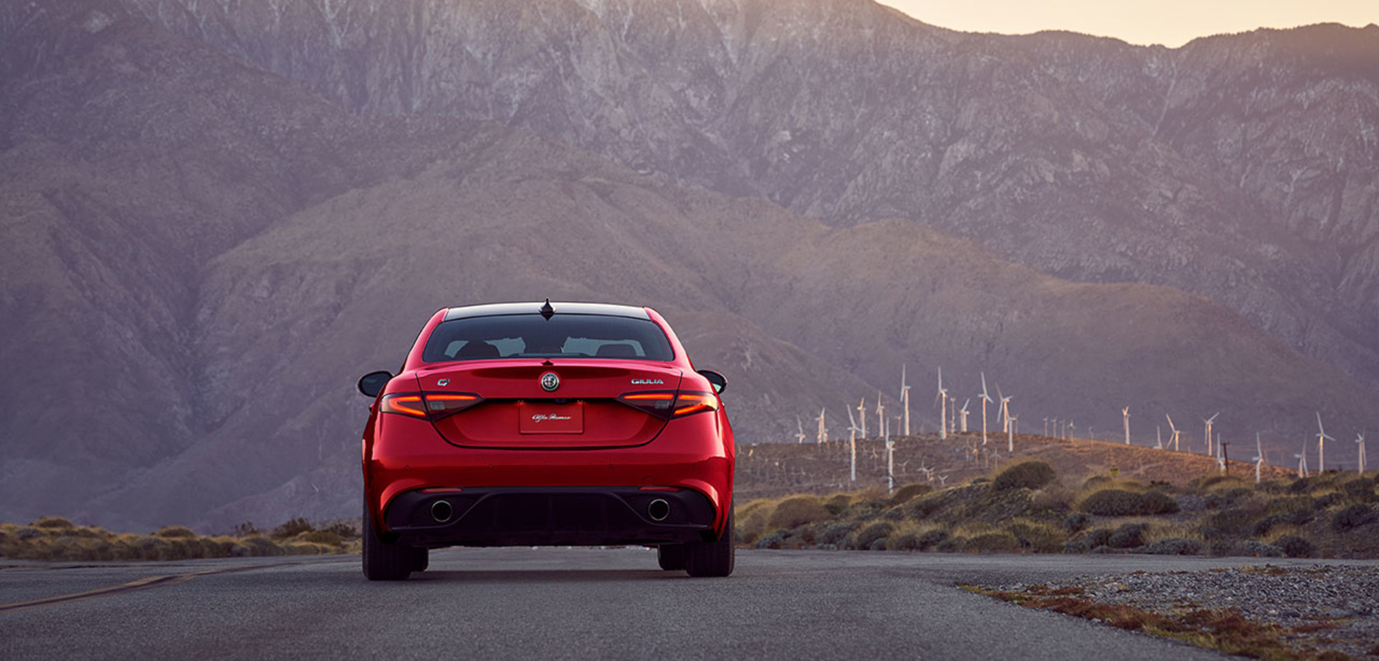 Rear view of a red 2026 Alfa Romeo Giulia with mountain backdrop at sunset.