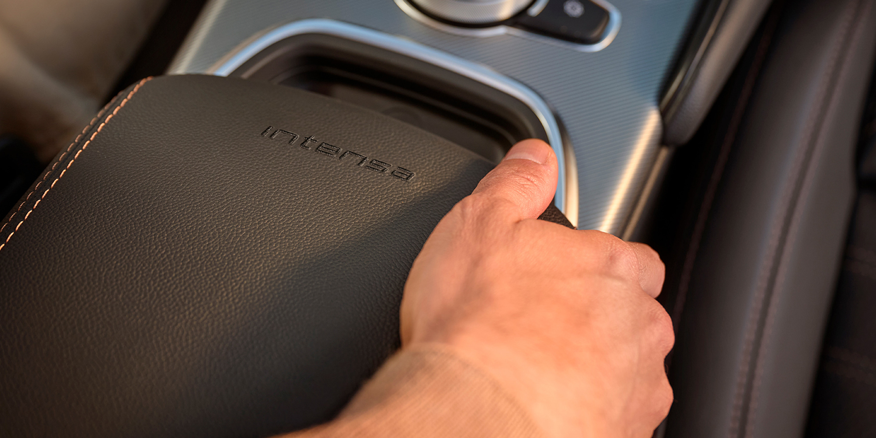 Un gros plan de la console centrale d’une voiture Alfa Romeo mettant en évidence une main reposant sur un accoudoir en cuir avec Intensa brodé sur celui-ci.  
