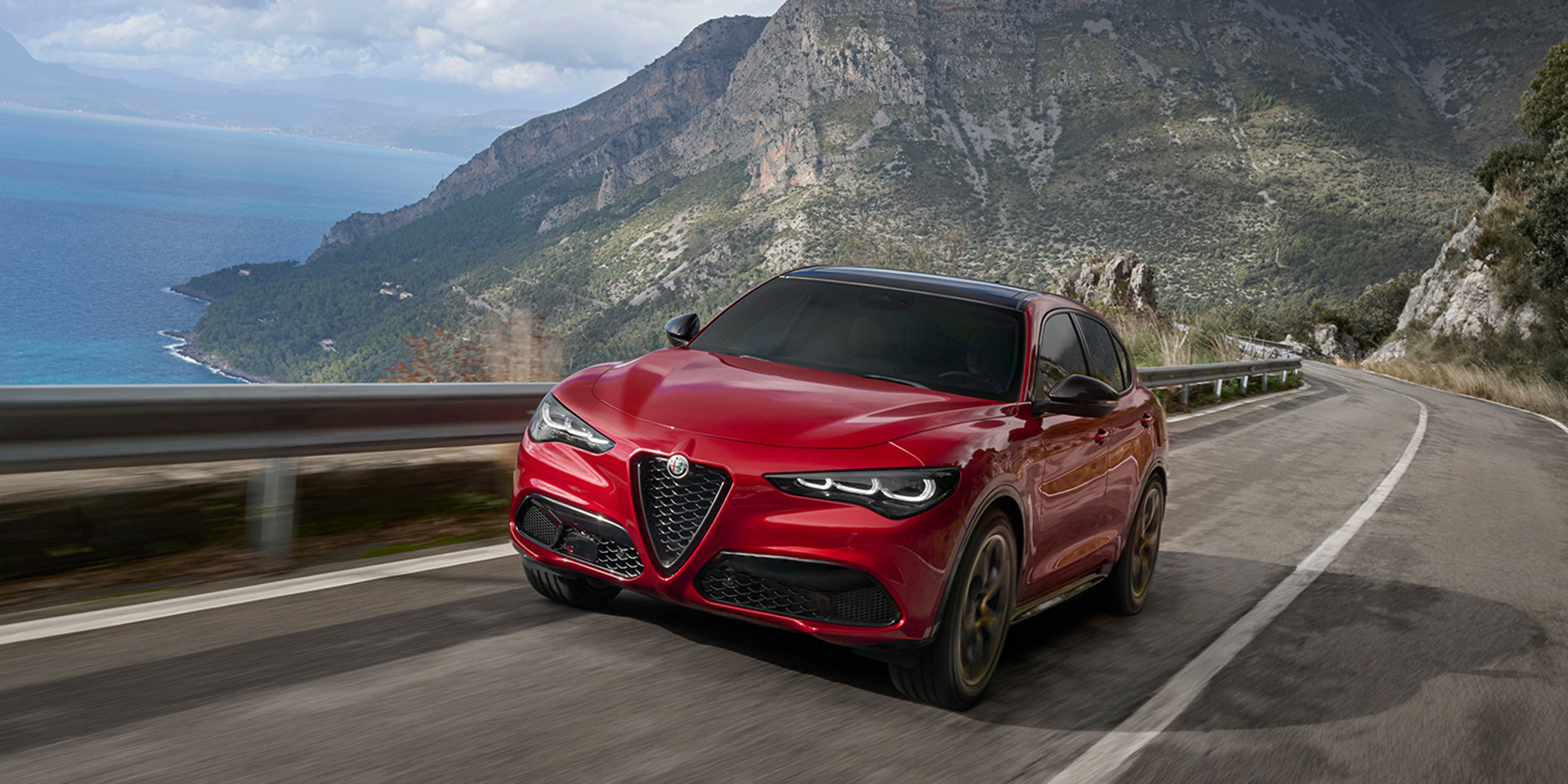 Une voiture Alfa Romeo rouge qui roule le long d’une route côtière pittoresque.