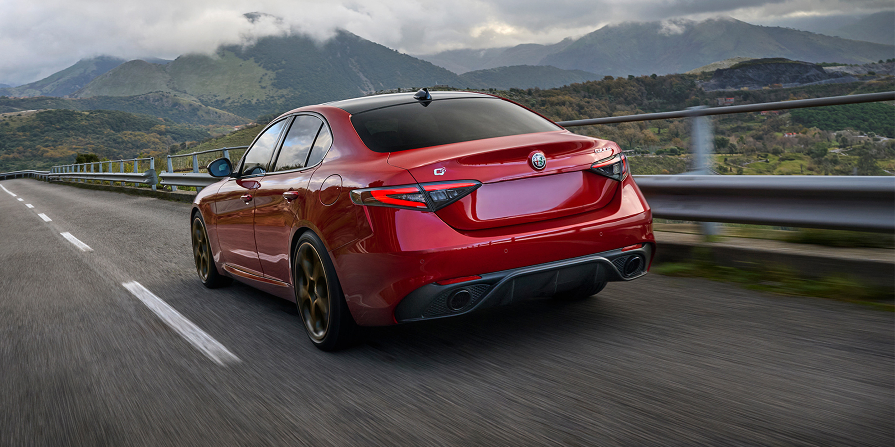 Une voiture Alfa Romeo rouge roulant sur une route de montagne sinueuse mettant en valeur son design élégant et aérodynamique.