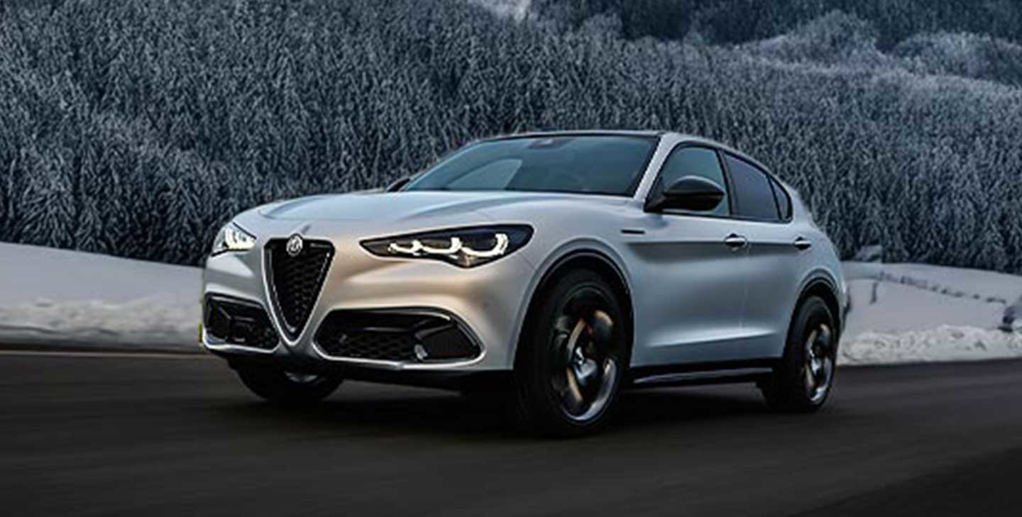 Une Alfa Romeo grise 2025 roulant sur une route avec des arbres enneigés en arrière-plan.