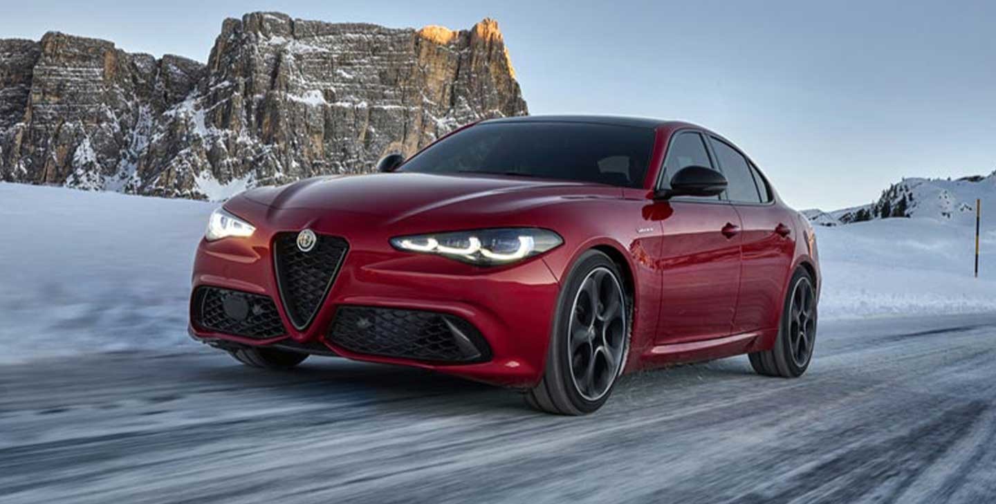 Une Alfa Romeo rouge 2025 roulant sur une route enneigée avec des falaises rocheuses en arrière-plan.