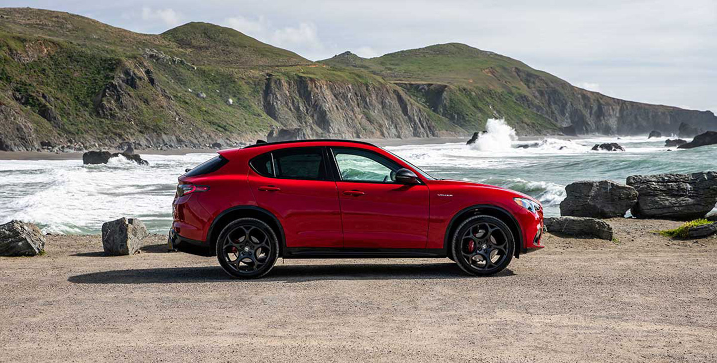 Profile view of a red Alfa Romeo SUV parked on a gravel shore.