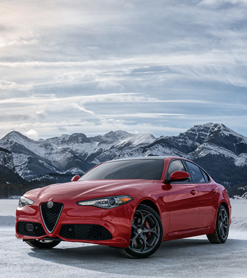 Red Alfa Romeo parked by a winter landscape with majestic mountains in the distance.