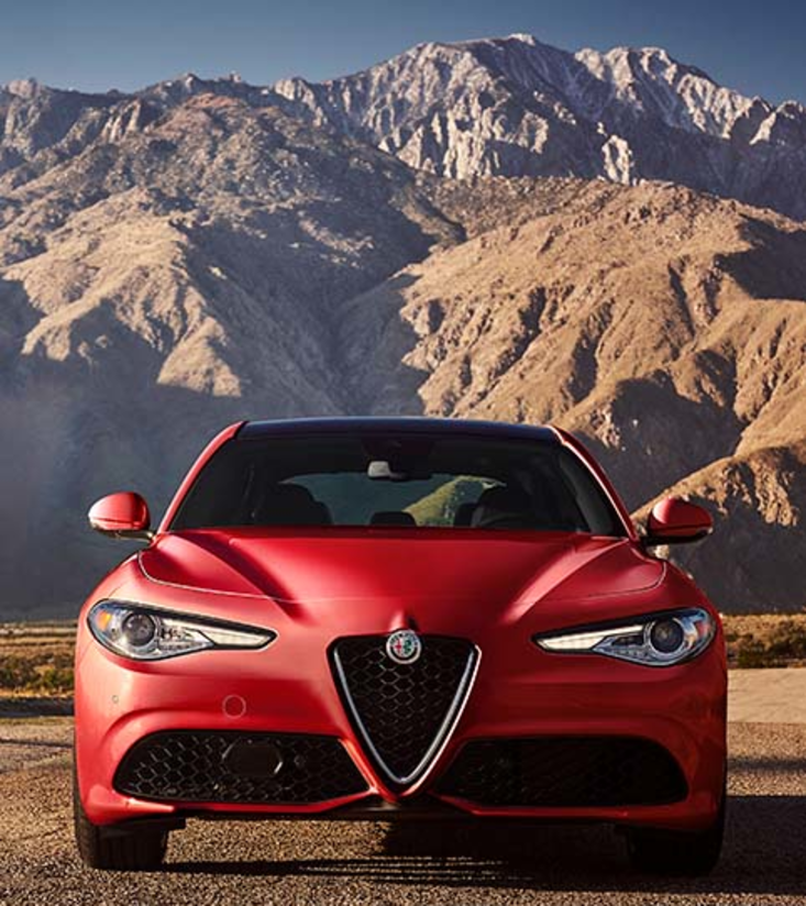 Alfa Romeo rouge garée dans un paysage hivernal avec de majestueuses montagnes au loin.