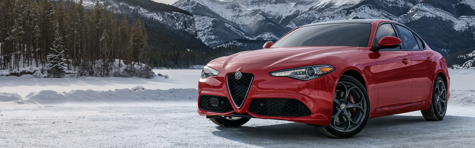 Giulia Ti in Alfa Rosso parked in snowy field, mountains behind