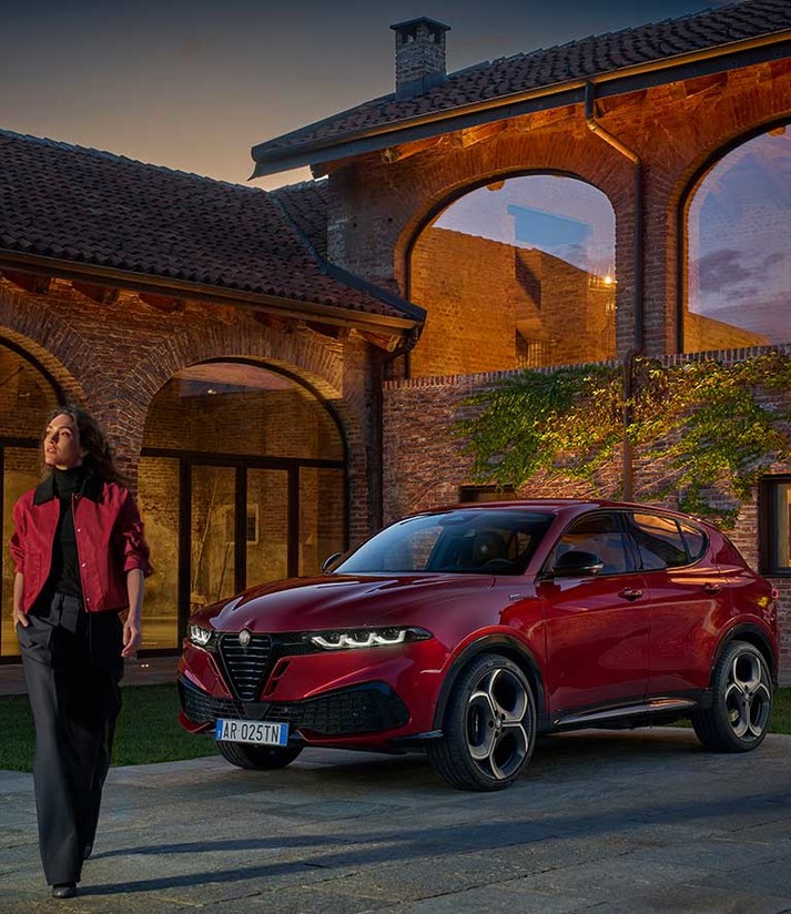 Une Alfa Romeo Tonale garée sur le trottoir près d'un bâtiment alors qu'une femme s'éloigne du véhicule.