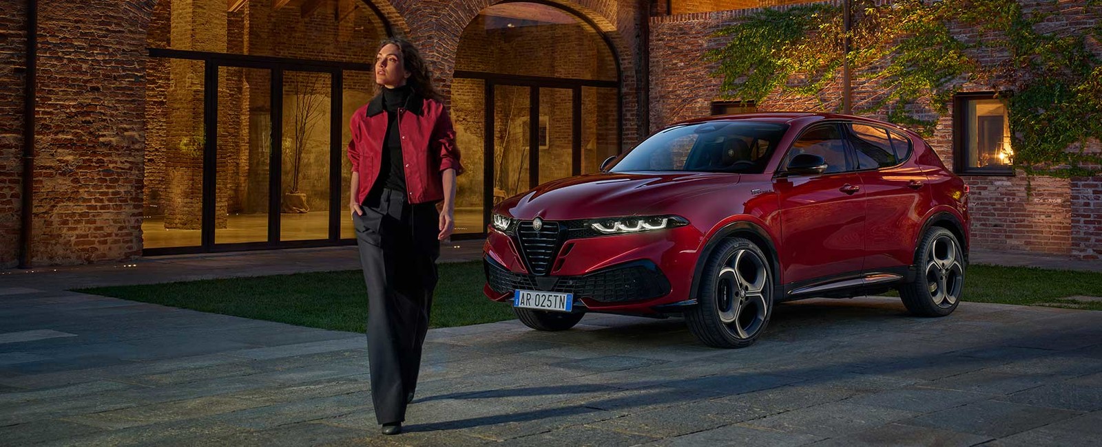 Une Alfa Romeo Tonale garée sur le trottoir près d'un bâtiment alors qu'une femme s'éloigne du véhicule.