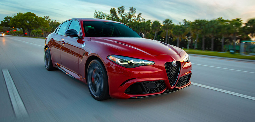 Une Alfa Romeo Giulia Quadrofoglio 2024 rouge roulant sur une route avec des arbres verts en arrière-plan.