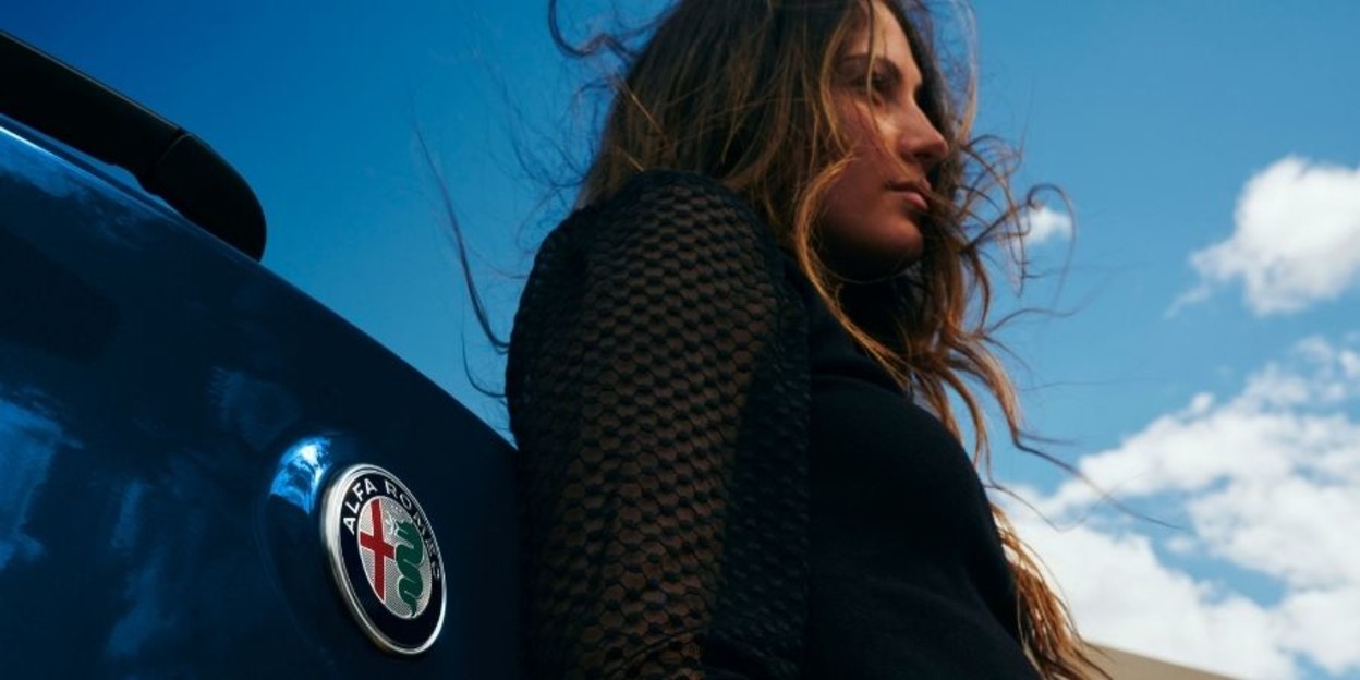 Red 2025 Alfa Romeo electric vehicle plugged into a wall-mounted EV charger on the exterior of a modern home. Shop The Collection