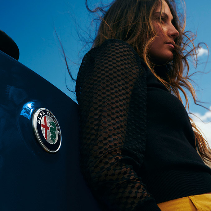 Une femme adossée à un Stelvio bleu 2022 présentant son logo