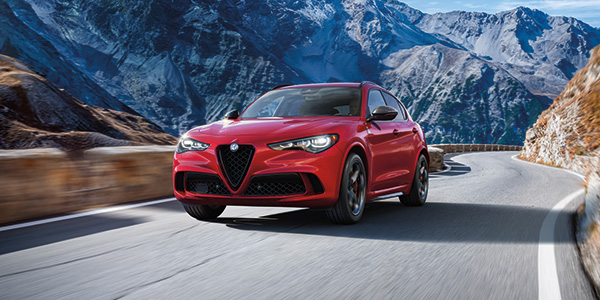 Une Alfa Romeo Stelvio 2024 rouge roulant à vive allure sur la route avec des montagnes en arrière-plan.