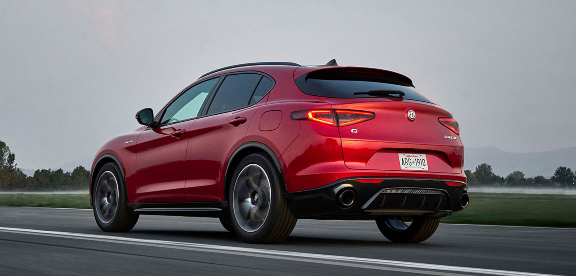 Vue arrière d'une Alfa Romeo Stelvio 2025 rouge roulant sur une route pavée.