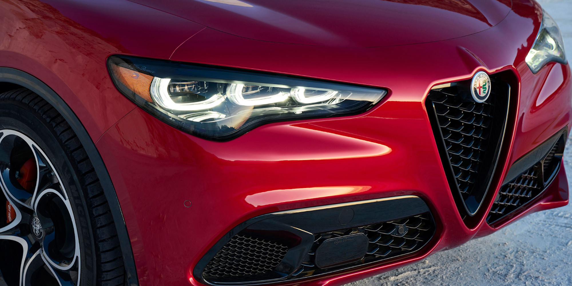 Gros plan d'une Alfa Romeo Stelvio rouge 2025, mettant en valeur la calandre avant élégante et les phares distinctifs.