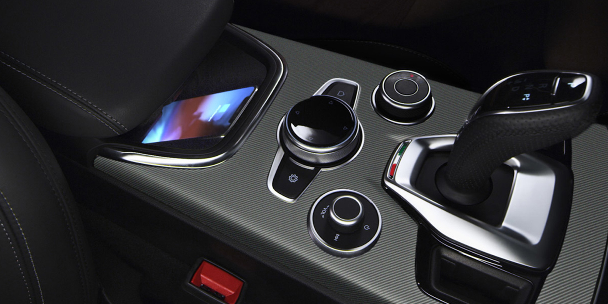 Vue intérieure d'un véhicule Alfa Romeo 2025 doté d'une console centrale sophistiquée. L'image met en valeur un socle de chargement sans fil avec un appareil placé dessus, ainsi que des boutons de commande au design élégant et un levier de vitesses épuré.