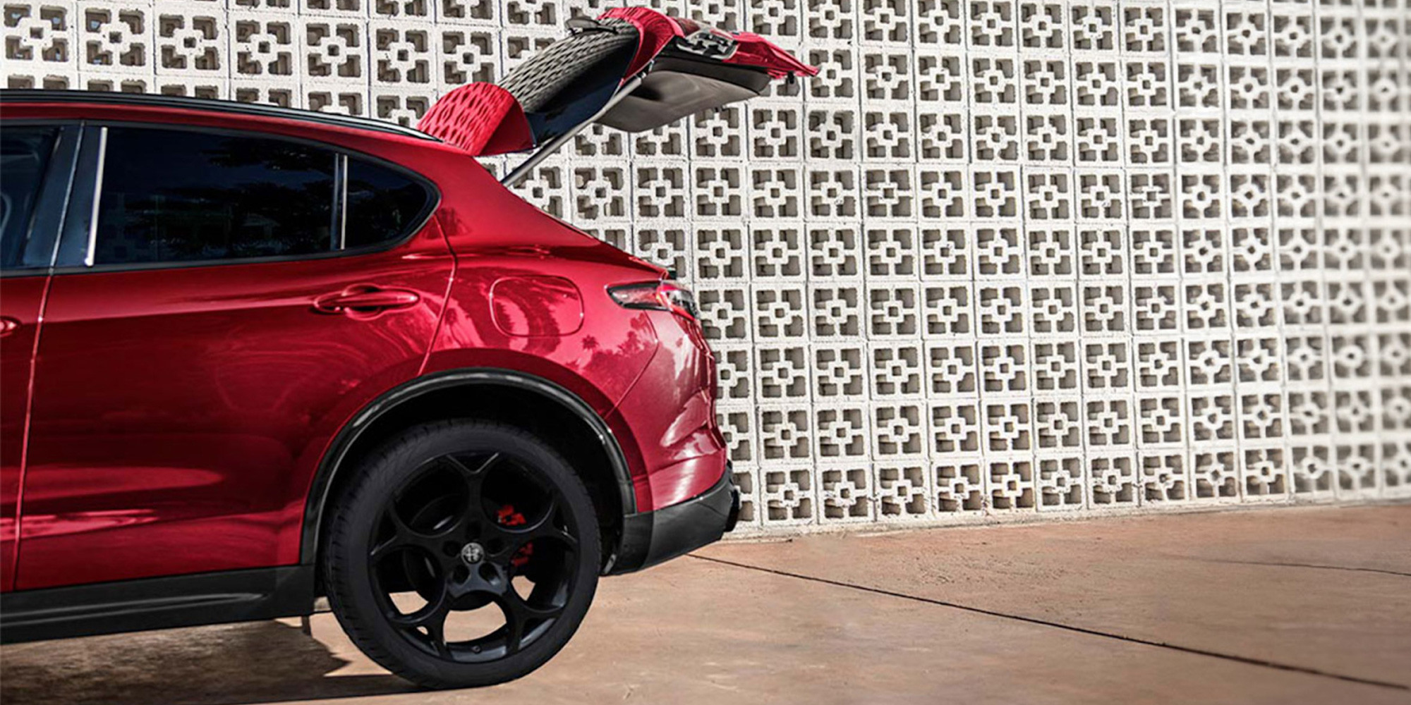 Vue partielle d'une Alfa Romeo rouge 2025 avec le hayon arrière ouvert et posé contre un mur texturé.