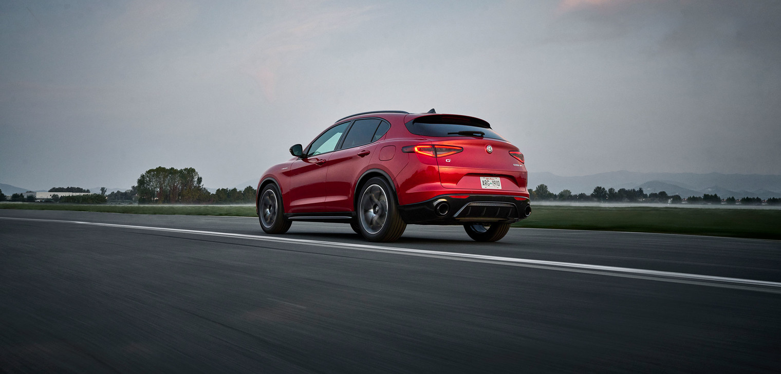 A front view of a red 2025 Alfa Romeo Stelvio shown driving on paved roadway with mountain terrain seen behind.