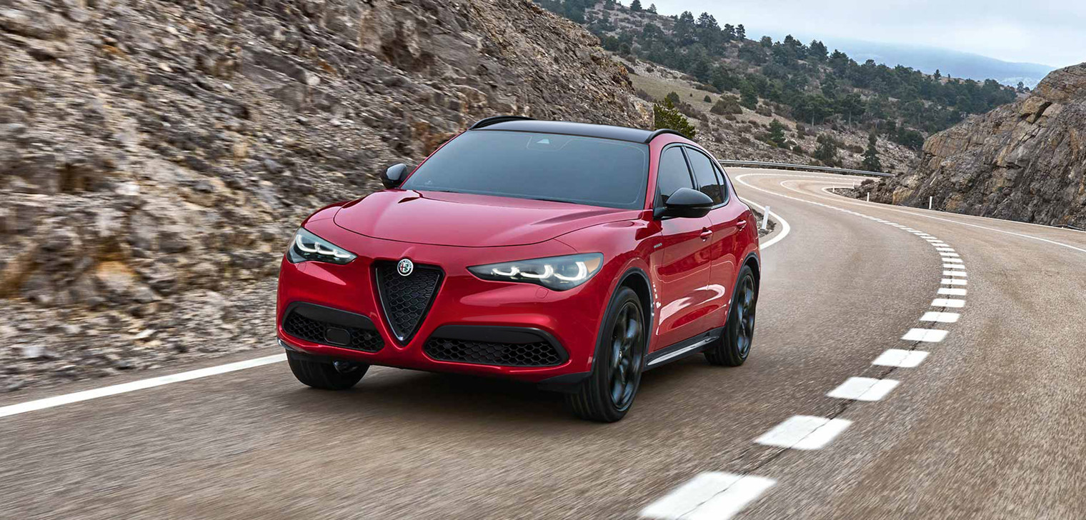 A back angled view of a red 2025 Alfa Romeo Stelvio shown driving on paved roadway.