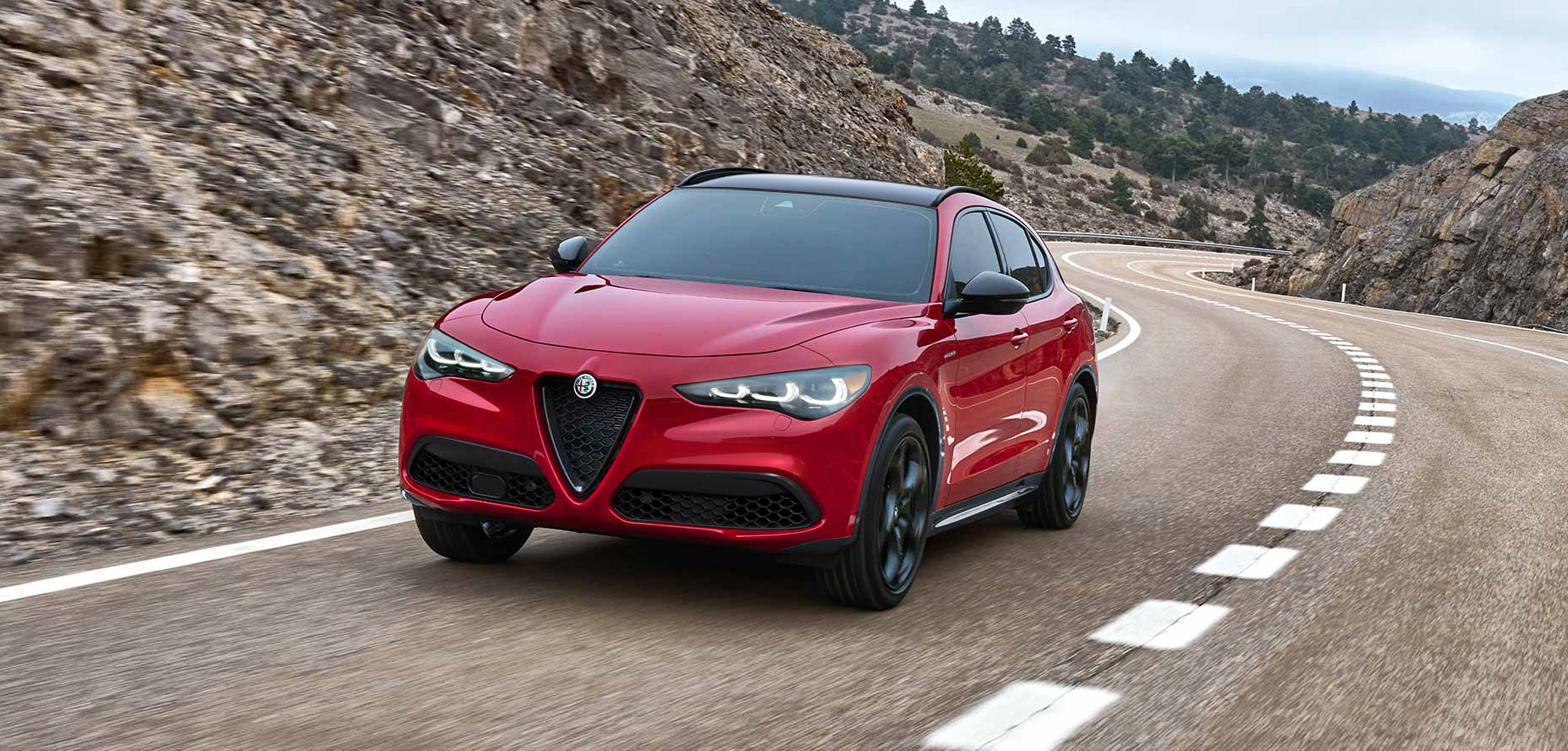 Vue en angle arrière d'une Alfa Romeo Stelvio 2025 rouge montrant une conduite sur une route pavée.