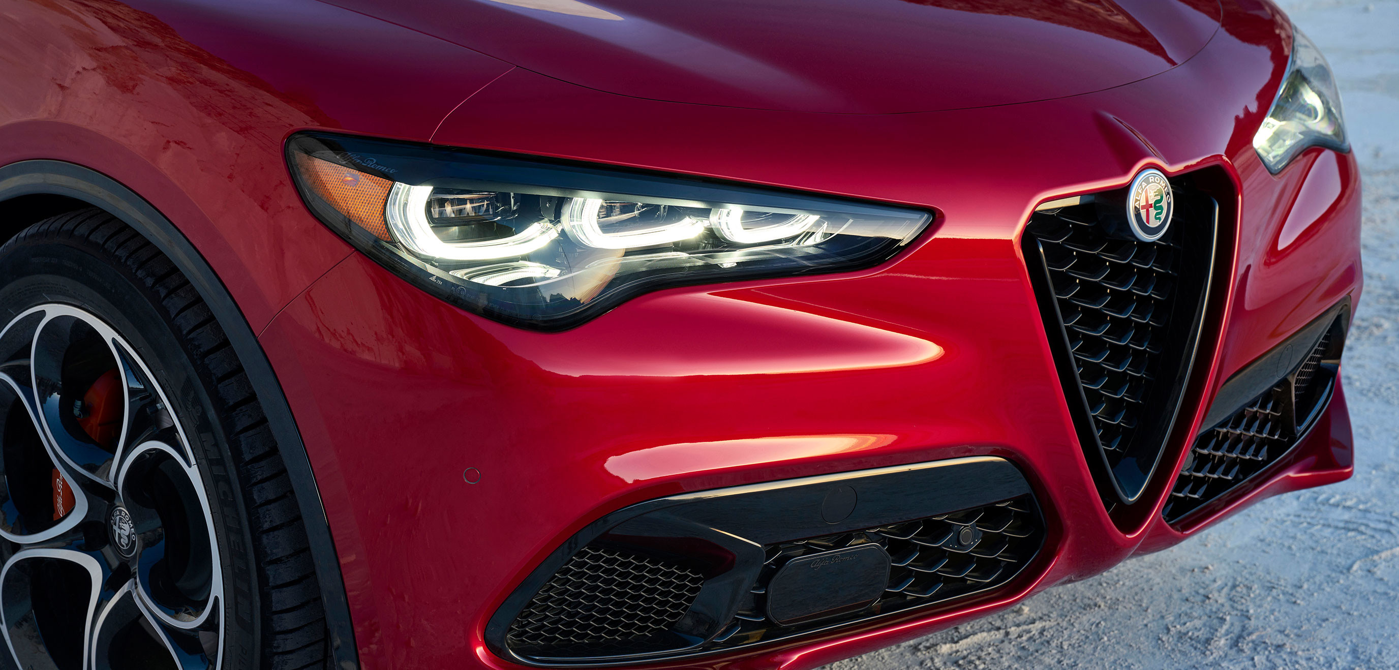 Vue de face d'une Alfa Romeo Stelvio 2025 rouge avec les phares allumés.