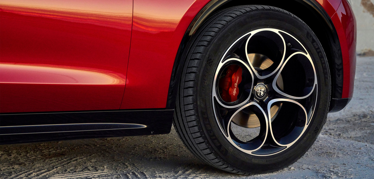 A close-up view of the front right wheel on a red 2025 Alfa Romeo Stelvio.