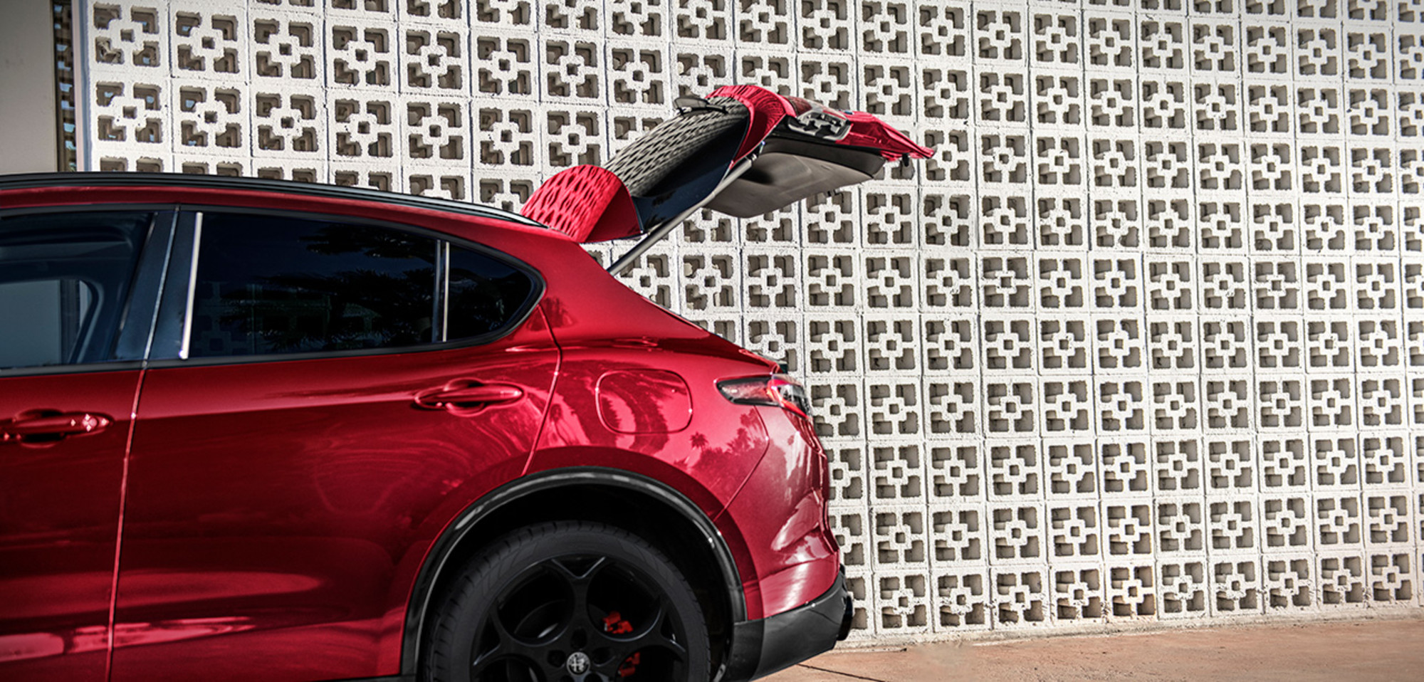 A partial view of a red 2026 Alfa Romeo Stelvio with the trunk gate lifted open.
