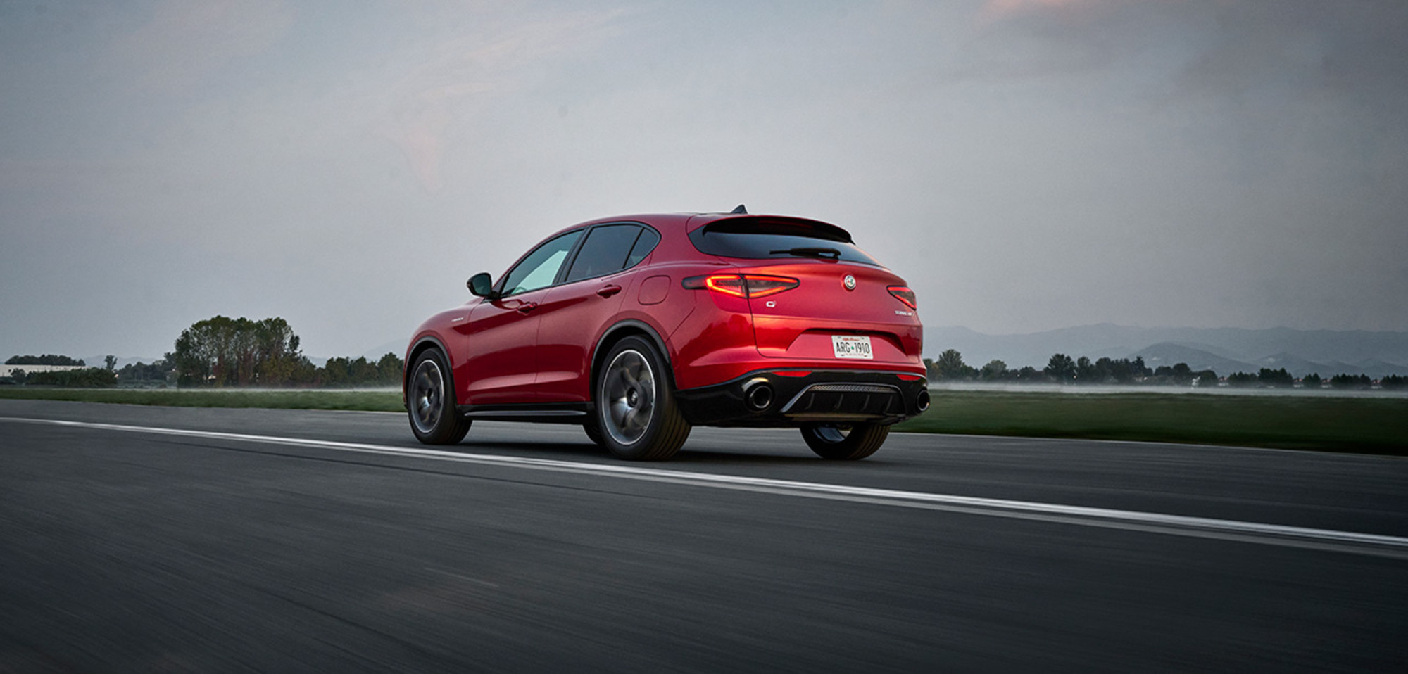 A back view of a red 2026 Alfa Romeo Stelvio in motion on a highway, featuring its rear sport diffuser. 